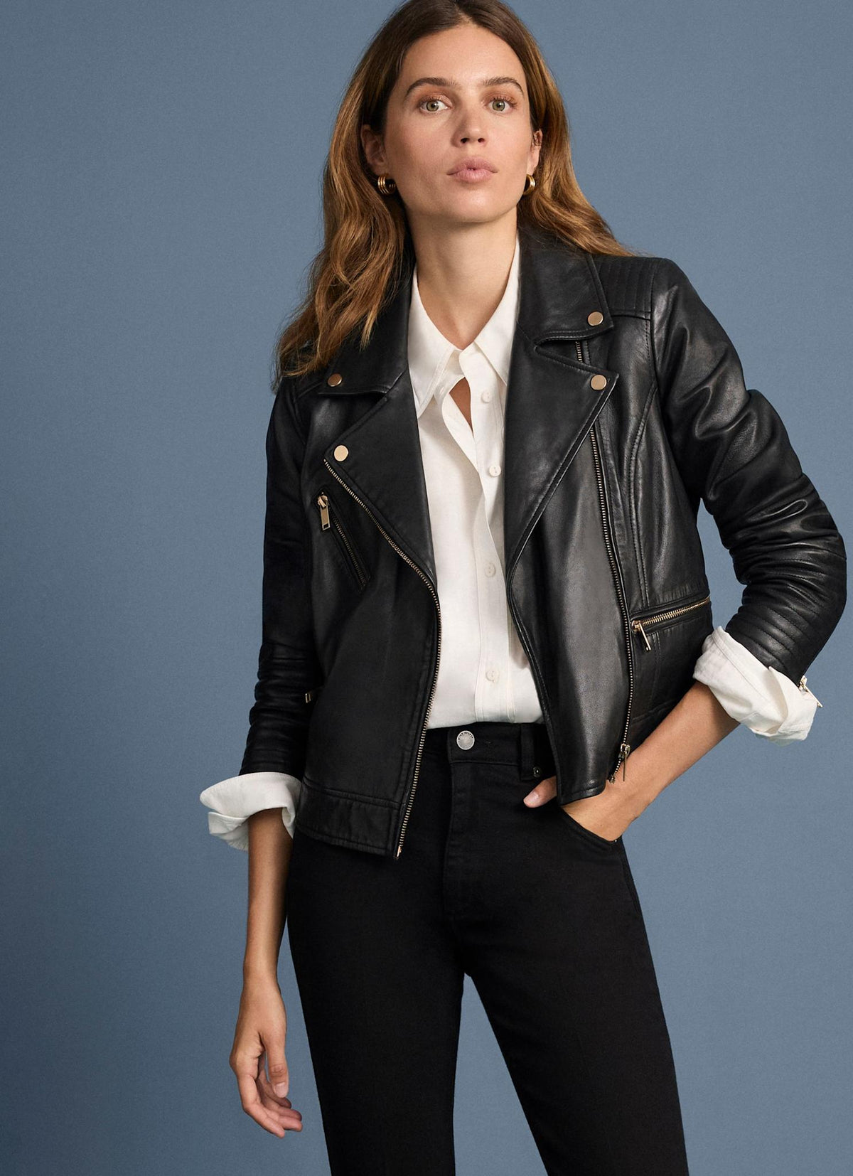 Woman wearing a black leather jacket over a white shirt against a blue background