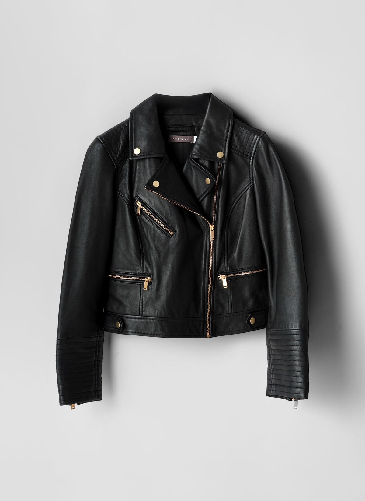 Black leather jacket with gold zippers on a light gray background