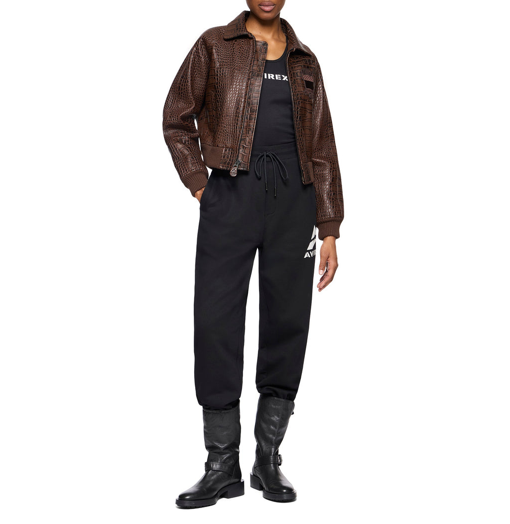 A model wearing a brown crocodile-embossed faux-leather jacket over a black top, black sweatpants with a white logo, and black boots, shot against a solid white background.