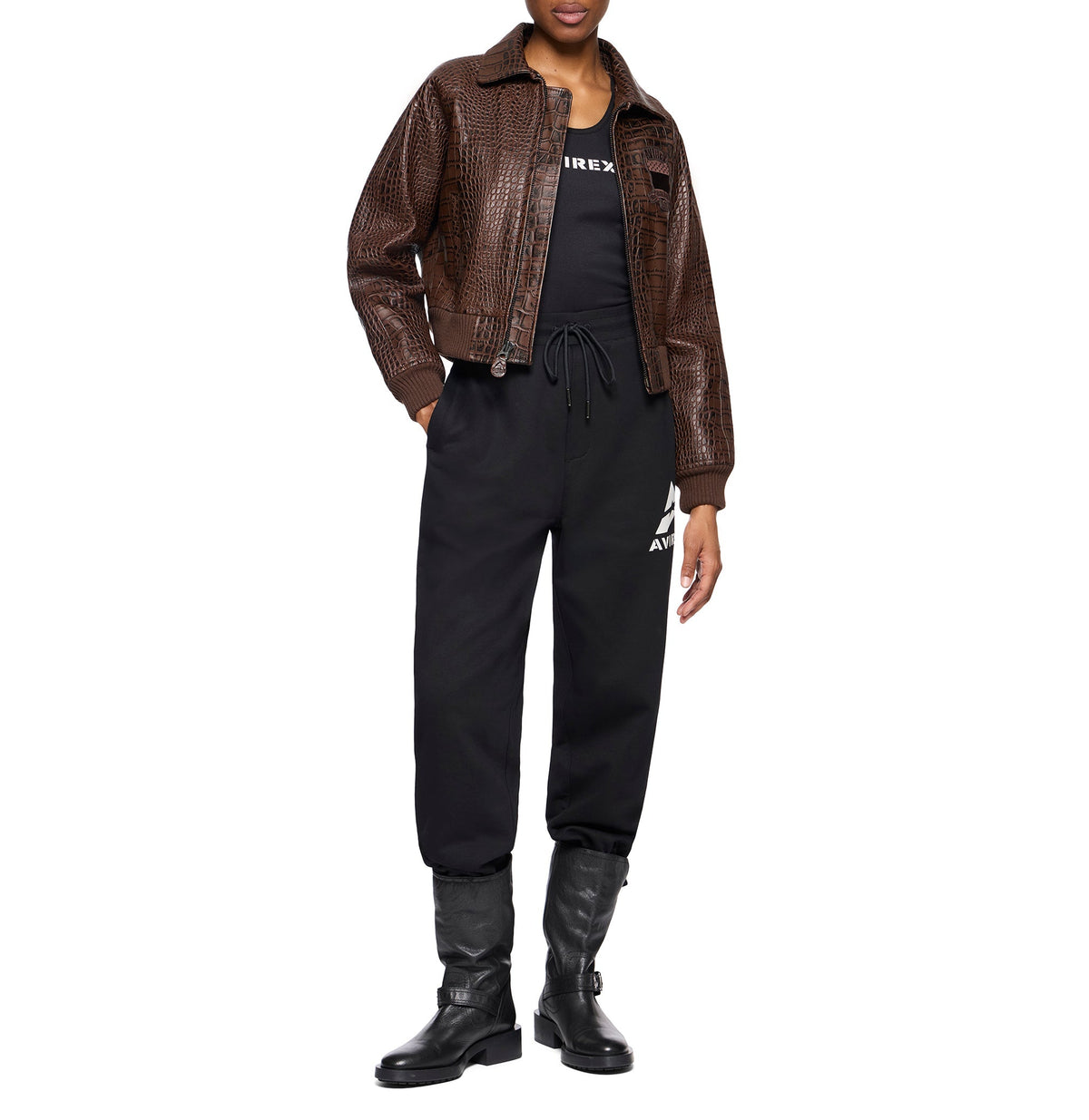 A model wearing a brown crocodile-embossed faux-leather jacket over a black top, black sweatpants with a white logo, and black boots, shot against a solid white background.