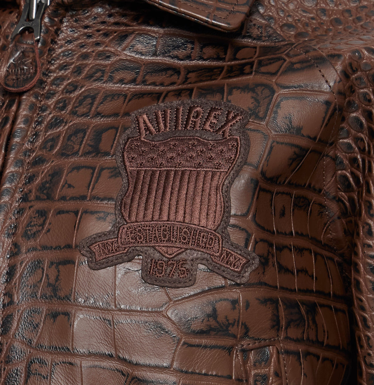 Close-up of a brown crocodile-embossed leather surface with a central embossed patch reading 'ANNA REX ESTABLISHED 1975'.
