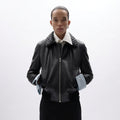 A model wearing a black leather jacket with a distinctive quilted collar, a white shirt underneath, and light blue shirt cuffs, set against a plain white studio background.