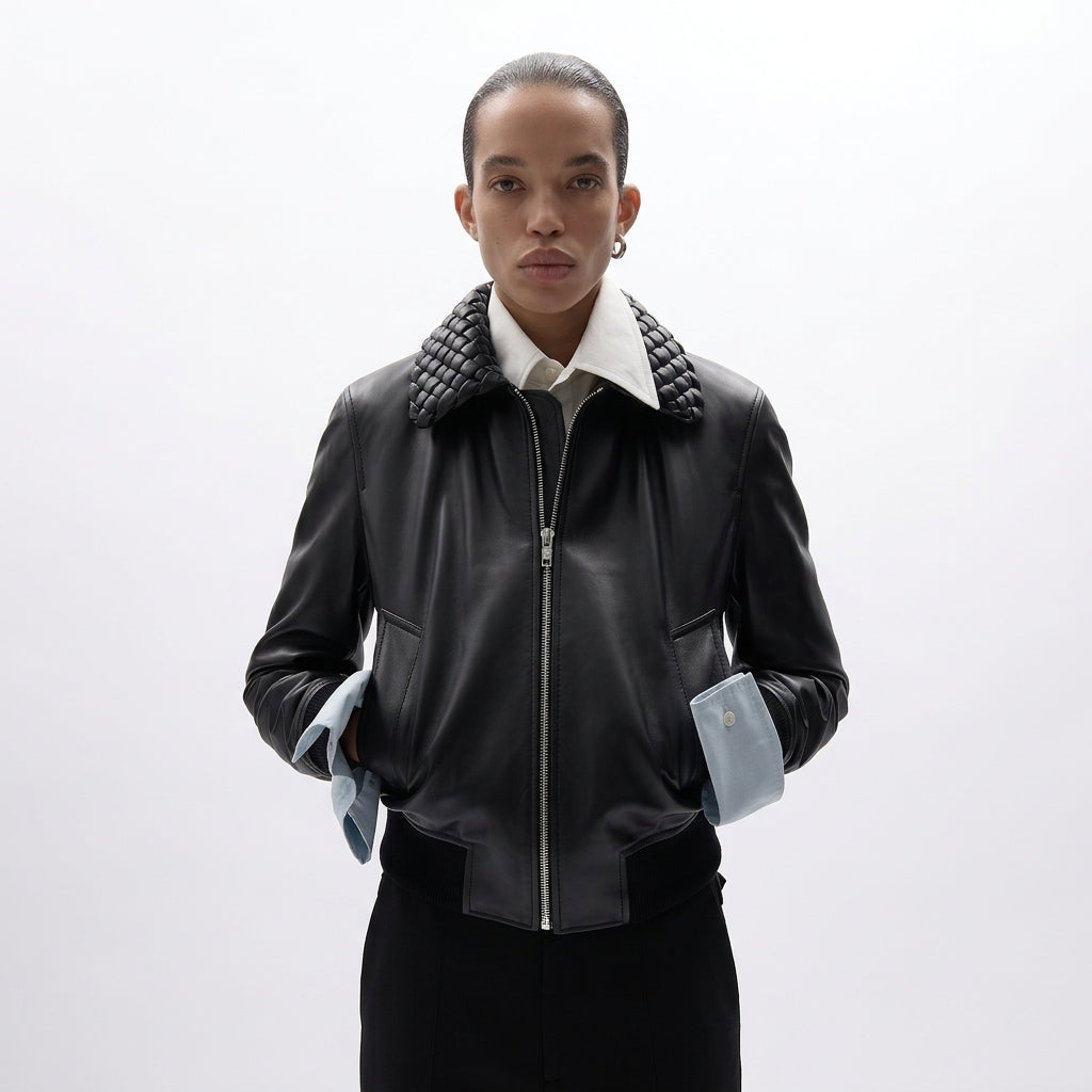 A model wearing a black leather jacket with a distinctive quilted collar, a white shirt underneath, and light blue shirt cuffs, set against a plain white studio background.