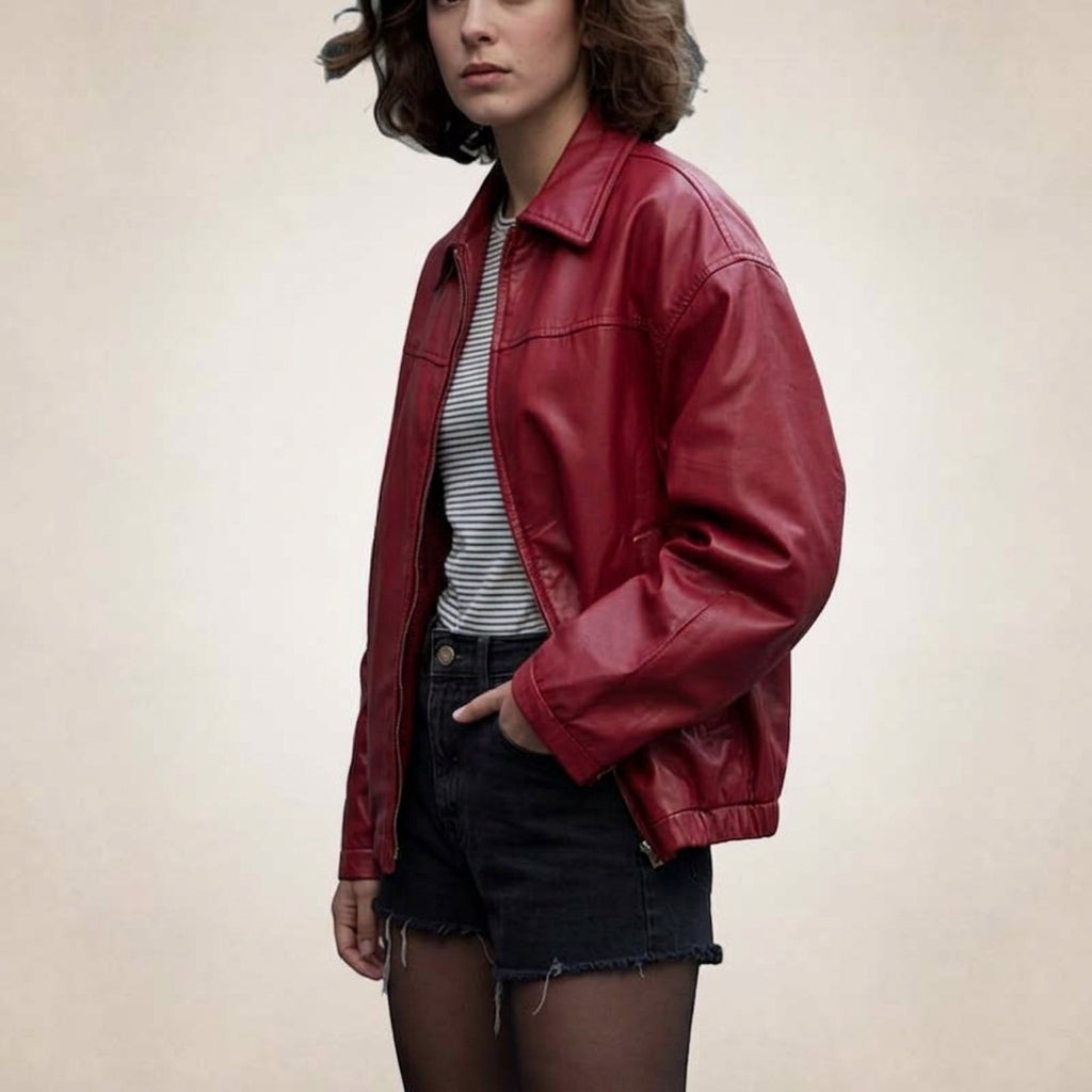 A woman wearing an oversized red leather jacket over a gray and white striped t-shirt, paired with dark denim shorts, standing against a plain beige background.