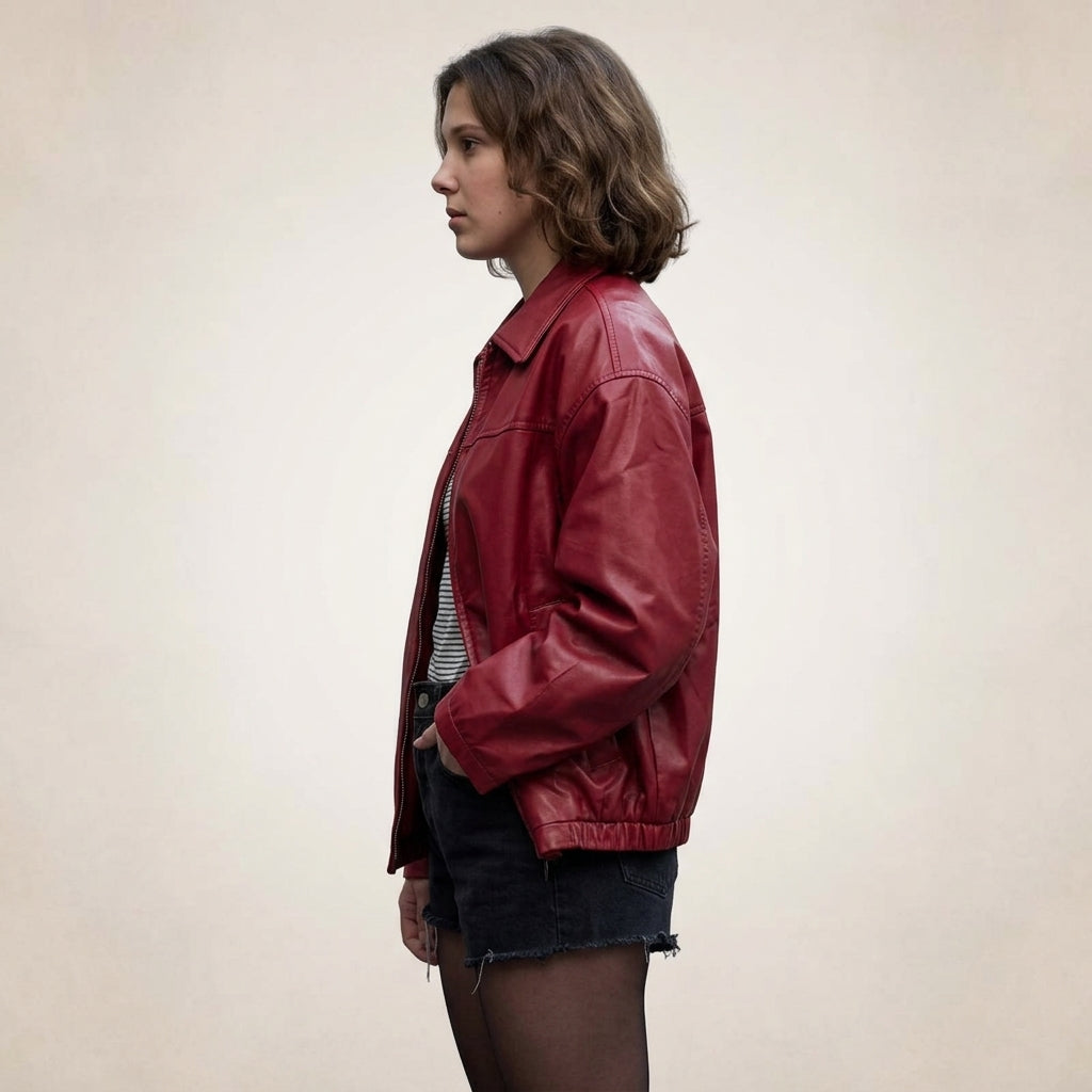 A woman in profile wearing a red leather jacket over a striped shirt and denim shorts, standing against a plain light beige background.