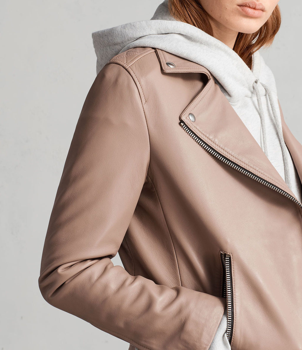 Close-up of a person wearing a beige leather jacket with a plain background