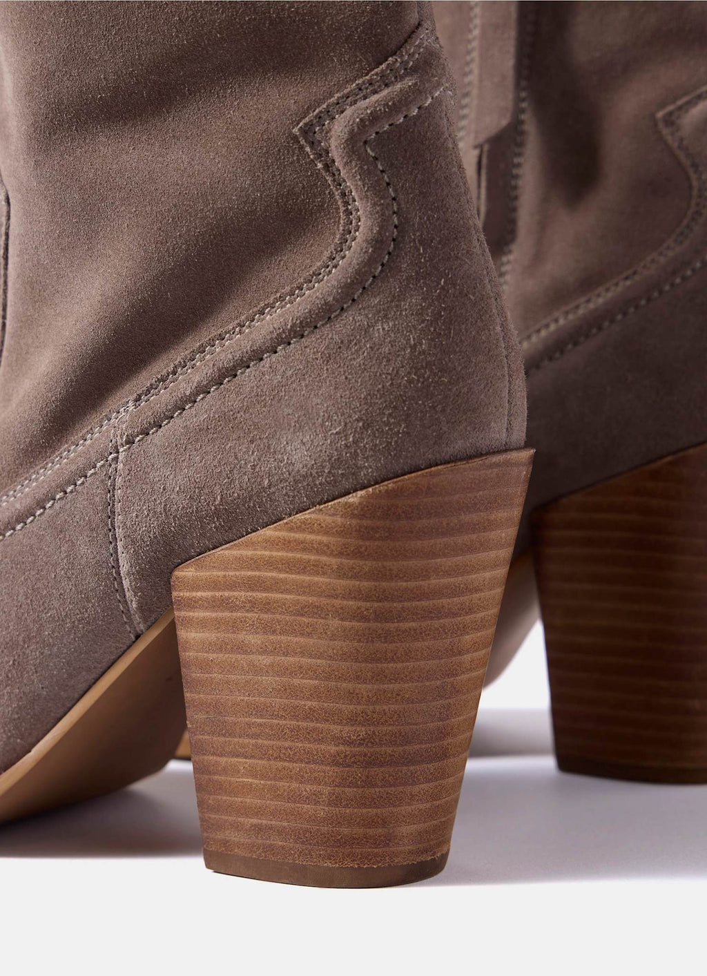 Close-up of the heel and back of a taupe-brown suede ankle boot with a chunky ribbed brown block heel, shown against a white background.