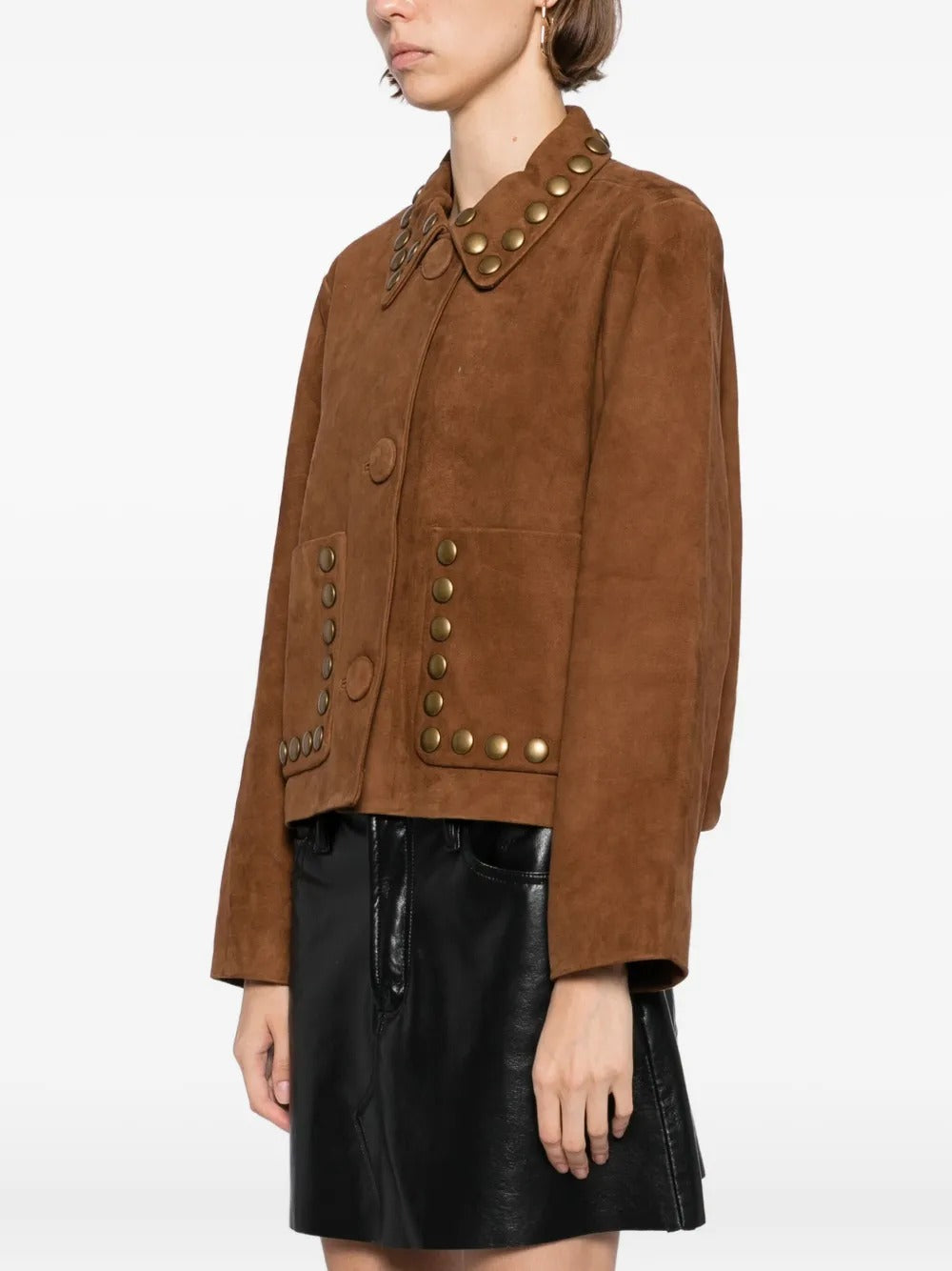 A model wearing a cropped brown suede jacket with brass-tone metal studs and a collar, paired with a black leather mini skirt, against a plain white studio background.