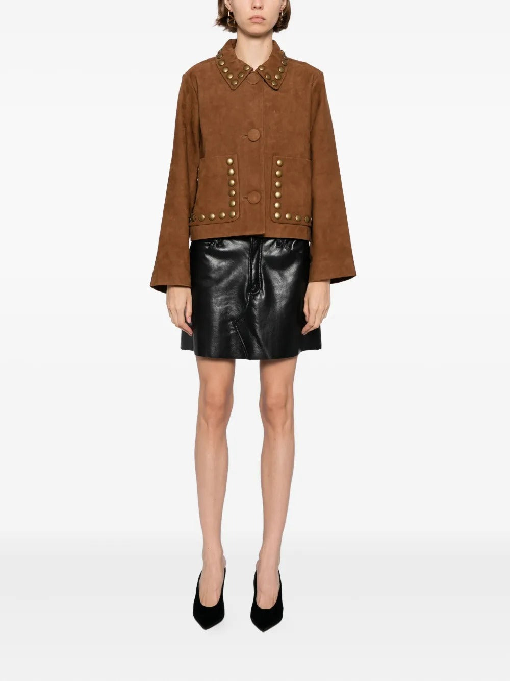 A model wearing a brown suede jacket with gold-tone metal studs and a black leather mini skirt, paired with black heels, shot against a plain white studio background.